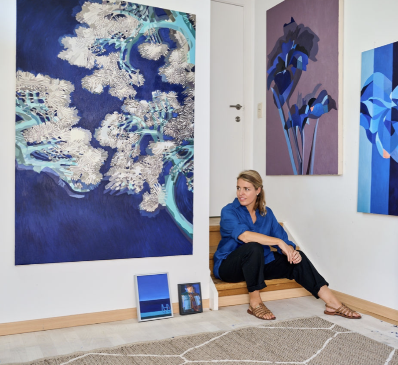Johanna Baudou in haar atelier, omringd door blauwe schilderijen met bloemenmotieven.